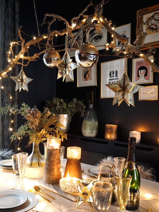 a woodland glam Christmas tablescape with shiny candleholders, greenery and a catchy chandelier made of a tree branch with lights, star and ball-shaped ornaments