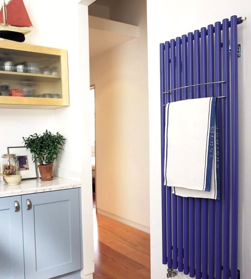 a catchy kitchen with pale blue and yellow cabinets, white stone countertops and a cobalt blue radiator on the wall