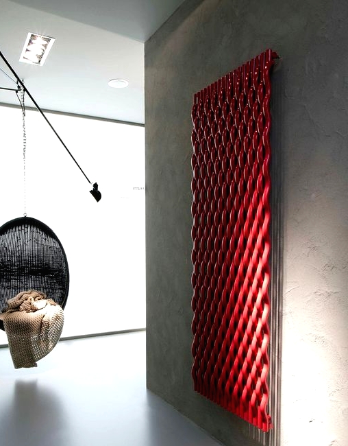 a contemporary space all done of concrete, with a black suspended chair and a red woven radiator on the wall is a pretty solution