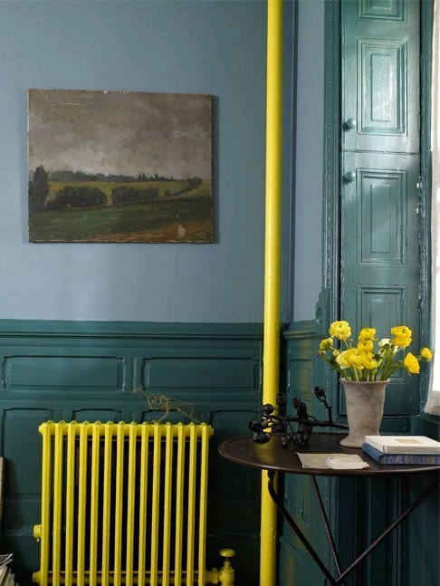 a moody vintage-inspired space with blue walls and dark green wainscoting, a neon yellow radiator and a tube, bold blooms