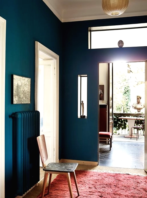 a navy entryway with white doors and framing, a matching navy radiator, a red rug and a simple chair is a chic space