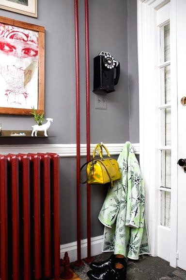 a small entryway with grey walls and grye rugs, a bold red radiator and tubes, a vintage phone and art that create a mood here