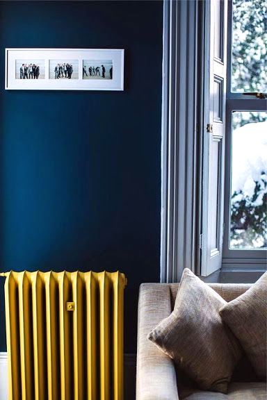 a stylish navy living room with white wainscoting, a grey sofa and a yellow radiator that adds color and a cheerful feel to the space
