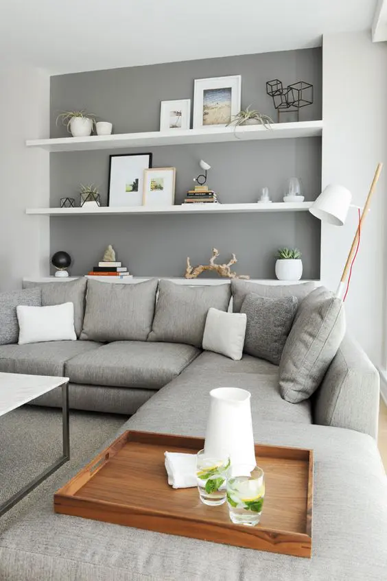 a neutral contemporary living room with a grey sectional, white floating shelves and a marble coffee table