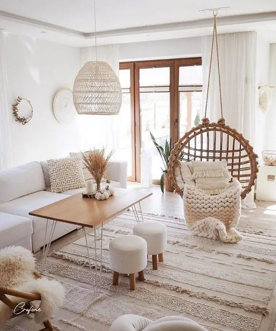 a neutral boho living room with a white sofa, a table with hairpin legs, a pendant chair, lovely rugs and blankets and a pendant lamp