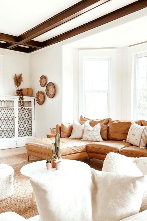 a welcoming boho living room with dark beams, a leather sofa, white furniture and decorative baskets on the wall