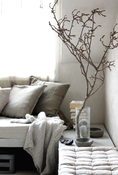 a very neutral wabi-sabi living room with a concrete bench, textural pillows and a blanket, a bench and some branches in a clear vase