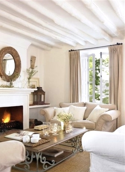 a neutral French farmhouse living room with whitewashed wooden beams, a fireplace, neutral seating furniture and a refined coffee table in the center
