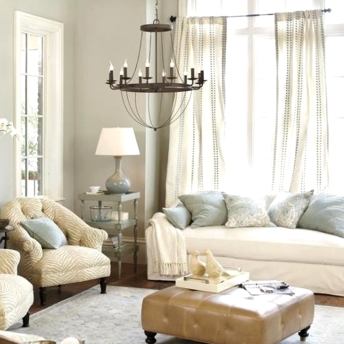 a chic neutral living room with grey walls, neutral seating furniture, a leather upholstered ottoman, a vintage chandelier and flowy curtains is very stylish