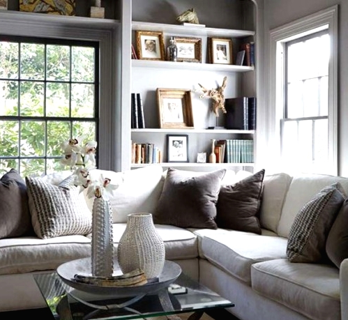 a cozy modern neutral living room with French windows, built-in shelves, a sectional and mismatching pillows, a glass coffee table and shiny metallic accents