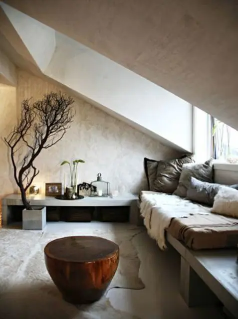 a neutral wabi-sabi living room with an attic ceiling and a window, concrete benches, a tree stump side table and some branches for decor
