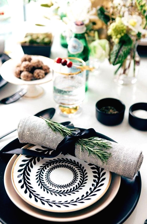a large black plate, a gilded one, a black and white printed plate on top and a burlap napkin with greenery for a chic Thanksgiving table