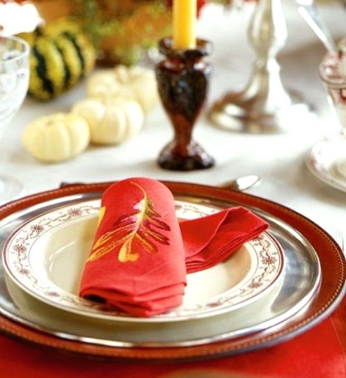a red, silver and printed plate, a red napkin with an embroidered leaf for a chic and bright fall or Thanksgiving place setting with a modern feel