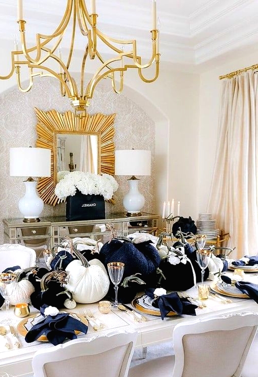 a glam Thanksgiving tablescape with large black and white velvet pumpkins, gold chargers, cutlery and candleholders plus black napkins