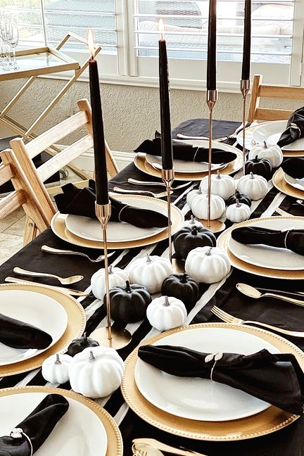 a lovely and refined Thanksgiving tablescape with a striped runner and black napkins, black and white pumpkins, tall and thin black candles and gold cutlery