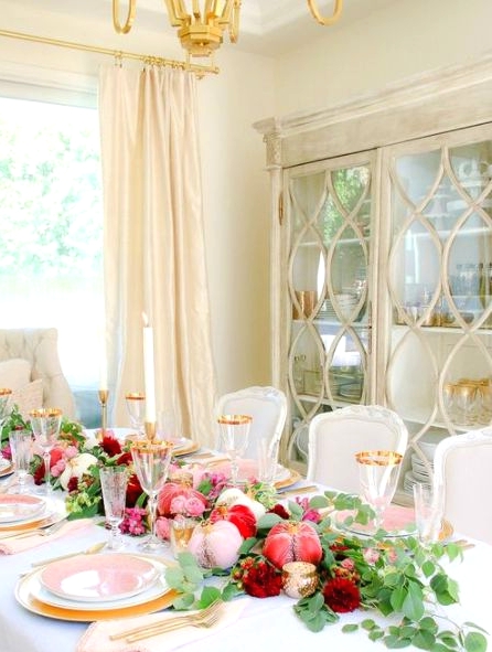 a lovely glam Thanksgiving tablescape with pink, blush, red velvet pumpkins, greenery, blush and white plates, gold cutlery and glasses with gold rims