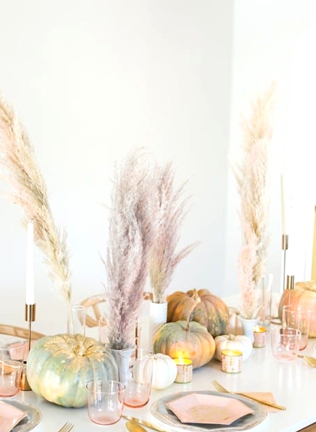 a modern glam Thanksgiving tablescape with pink plates, napkins, glasses, natural and pink grass, heirloom pumpkins and gold cutlery