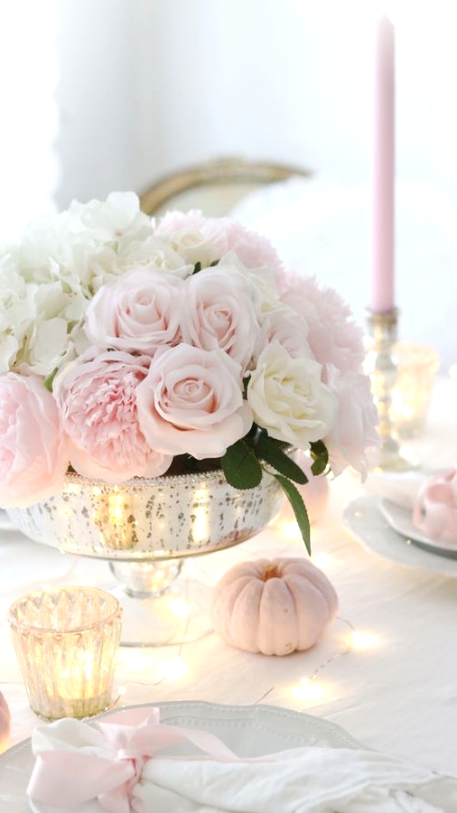 a refined and glam Thanksgiving tablescape with chic plates, neutral linens, blush pumpkins, blush and white florals and some lights and candles