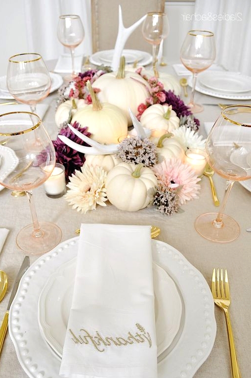 a lovely glam Thanksgiving tablescape with wihte pumpkins, antlers, blush, white and purple blooms, candles, white porcelain and blush glasses