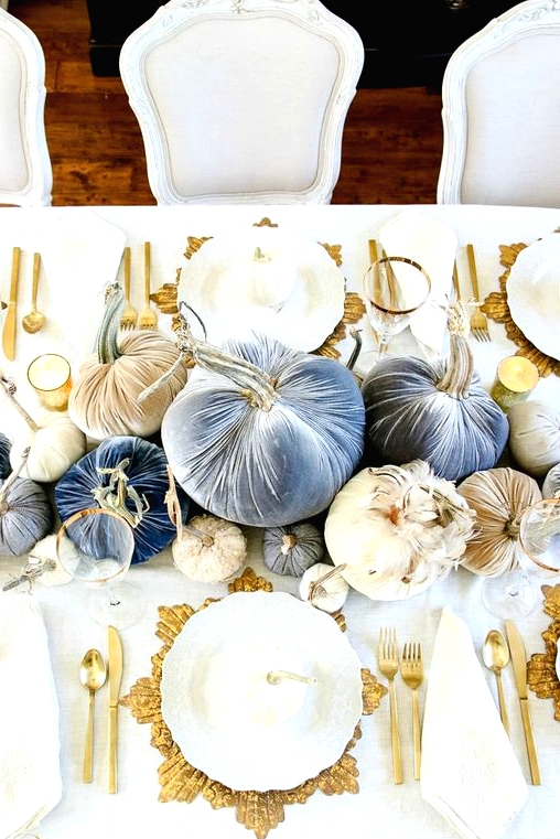 a sophisticated glam Thanksgiving tablescape with neutral, ligth blue and navy velvet pumpkins, gold chargers, cutlery and candles around
