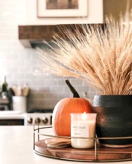 a simple fall or Thanksgiving decoration of a wooden tray with a pumpkin spice candle, a pumpkin and some wheat in a planter