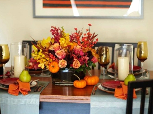 pillar candles accenting a bright floral Thanksgiving centerpiece creat e acozy ambience and invite everyone to the table