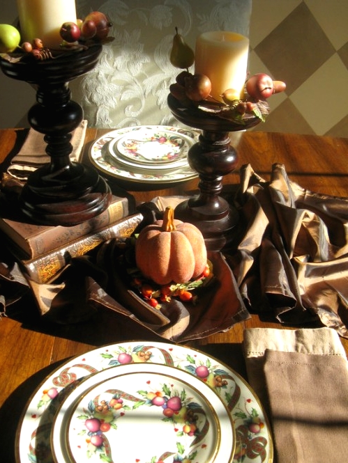a vintage rustic Thanksgiving centerpiece of dark stained candleholders, faux apples and pears and pillar candles plus a brown table runner and pumpkins
