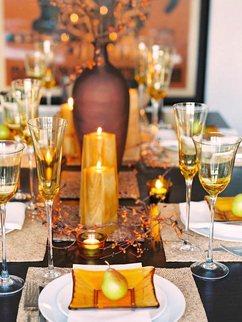 a rustic Thanksgiving centerpiece of amber pillar candles, branches and matching amber glasses and plates