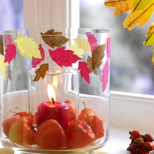a large glass with seed pods and colorful paper leaves attached plus a colored candle inside is a lovely decoration for fall or Thanksgiving