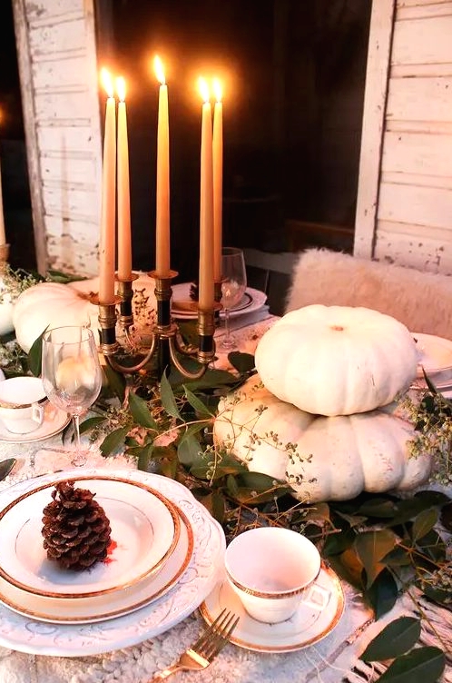 a natural Thanksgiving tablescape with white pumpkins, tall candles and a greenery runner plus pinecones is chic