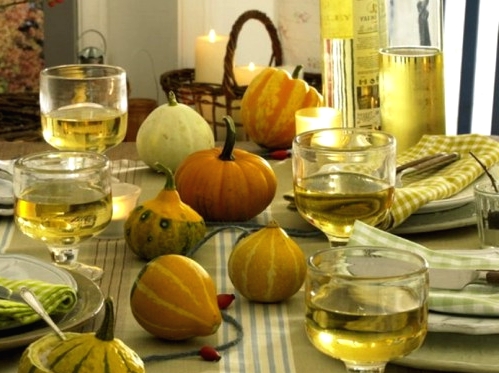a neutral and natural Thanksgiving tablescape with natural gourds and pumpkins, a green tablecloth and napkins, neutral porcelain and pillar candles