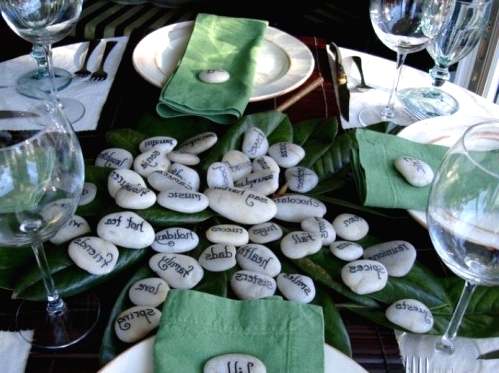 a simple Thanksgiving tablescape with green leaves and napkins, with pebbles that tell you what to sya thanks for