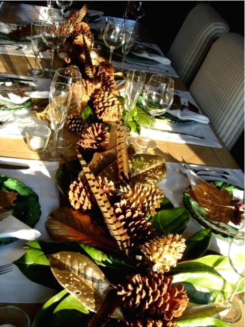 a natural Thanksgiving tablescape with green plates, a cool leaf runner with feathers and pinecones, gilded leaves accenting each place setting