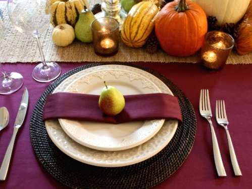 a bold and cool Thanksgiving table setting with natural veggies, pinecones, candles in candleholders and purple linens on the table