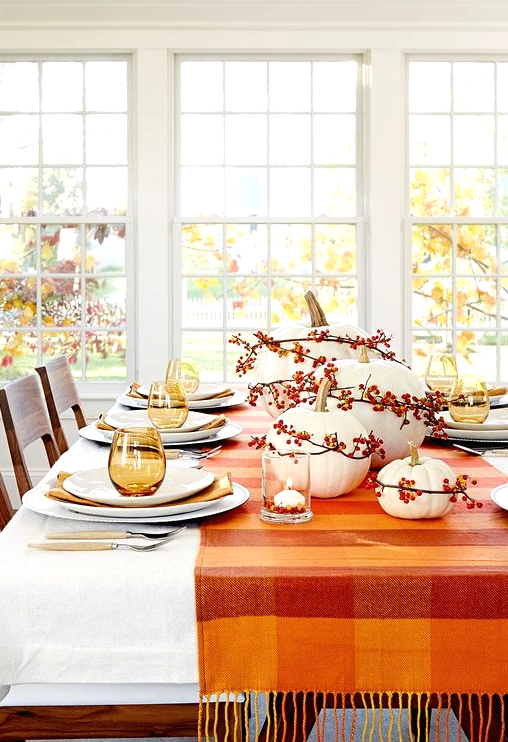 a cozy and simple Thanksgiving centerpiece of white pumpkins and bold berries accented with a bold matching table runner is a cool idea