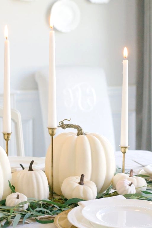 a super easy and cool Thanksgiving centerpiece of greenery, white pumpkins, tall and thin candles in gold candleholders is lovely
