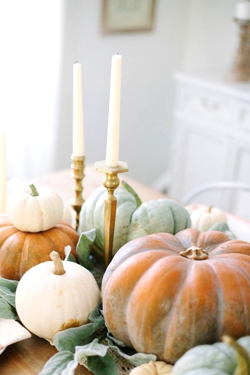a super natural Thanksgiving centerpiece of various natural pumpkins, foliage and tall and thin candles in elegant candlesticks