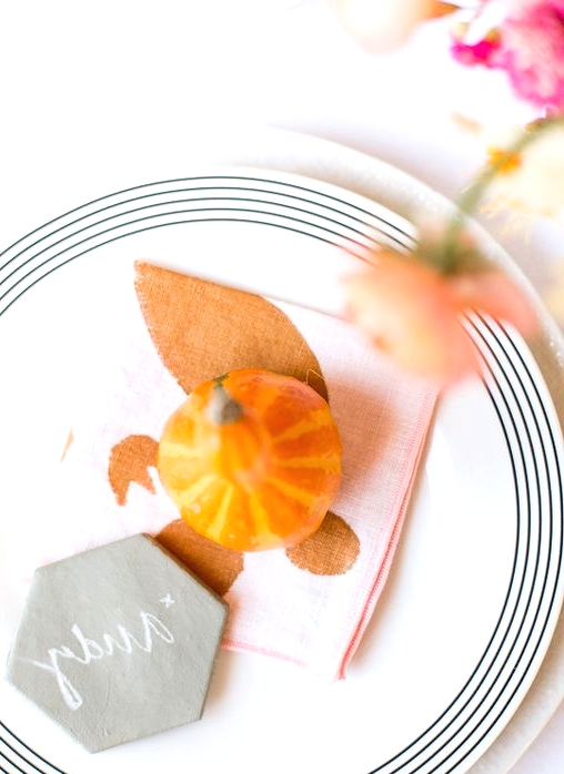 a very simple and lovely Thanksgiving place setting with a white and striped plate, a printed napkin, a gourd and a marble card