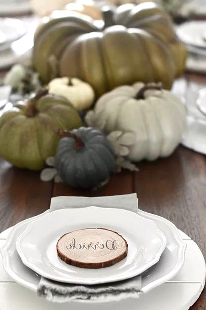 a very simple and stylish Thanksgiving place setting done with a white planked placemat and porcelain, a wood slice and a grye napkin