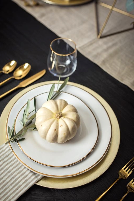 an elegant and chic Thanksgiving place setting with a gold charger, gold rimmed plates, gold cutlery and a striped napkin plus a pumpkin