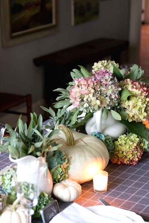 a delicate Thanksgiving centerpiece of green and pink hydrangeas, white pumpkins and some greenery in jugs