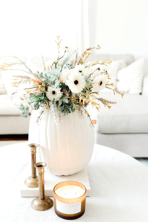 a neutral Thanksgiving centerpiece of a white pumpkin, white blooms, greenery and some blooming branches is cool