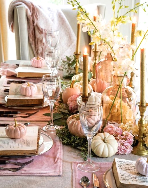 a pastel Thanksgiving centerpiece of pink blooms, greenery, pastel pumpkins and some amber vases and glitter candles is amazing