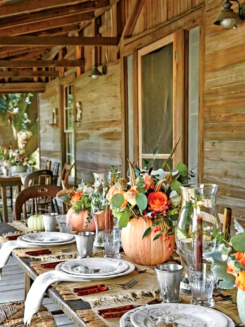 lovely bright Thanksgiving centerpieces of orange pumpkins, orange blooms and greenery, berries and feathers