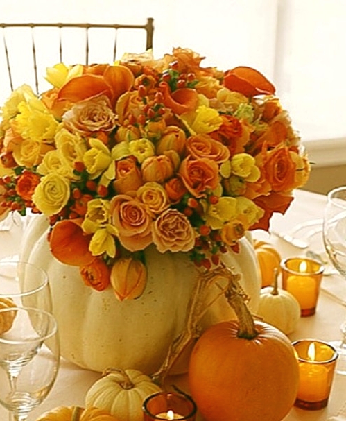 a bright fall or Thanksgiving centerpiece of a white pumpkin as a vase, orange, yellow and burgundy blooms plus berries is a cool and bold idea