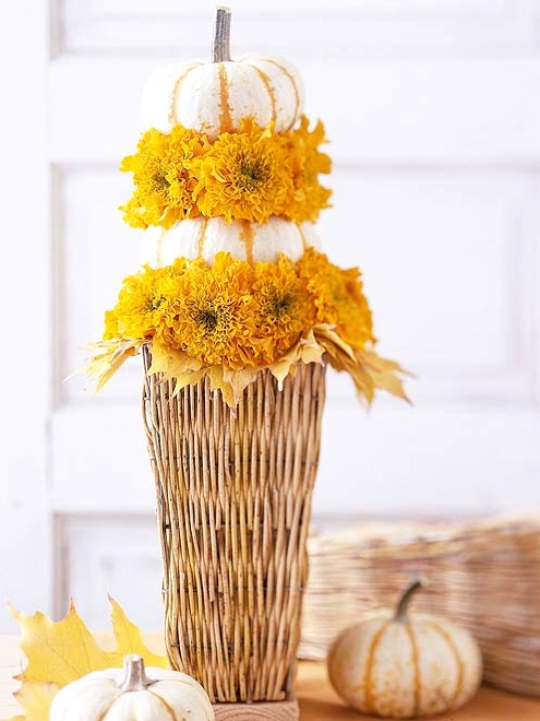a catchy rustic Thanksgiving centerpiece of a woven basket with yellow blooms and leaves and a couple of stacked white pumpkins is a catchy idea