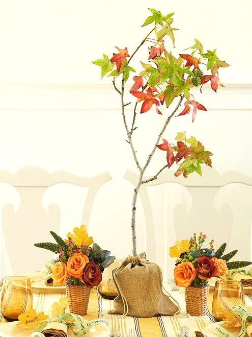 bright fall or Thanksgiving centerpieces of orange and burgundy blooms, succulents and berries and a burlap sack with a small tree with fall leaves
