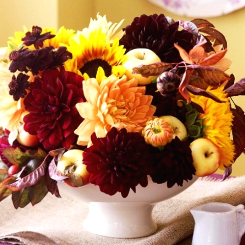 a bold fall or Thanksgiving floral and fruit centerpiece of yellow, orange and burgundy blooms, apples, dark foliage and artichokes is a catchy solution to rock