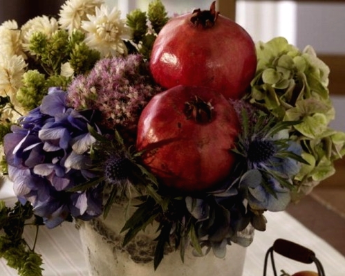 a bold fall or Thanksgiving centerpiece of a bucket, white, pink, green and purple blooms and pomegranates is a very catchy and decadent idea