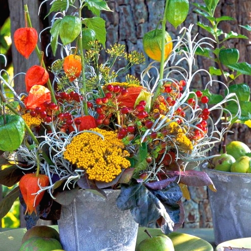 a bold and bright Thanksgiving centerpiece of a bucket with bold blooms, greenery, dried flowers, dark berries and dark foliage for a rustic celebration